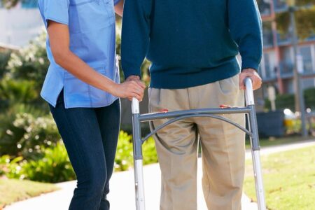 Perawatan lansia di rumah: seorang anggota keluarga membantu lansia berjalan dengan aman di dalam rumah